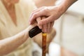 Woman holding senior`s hands leaning on walking cane