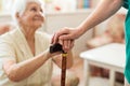 Woman holding senior`s hands leaning on walking cane