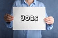 Woman holding sheet of paper with word JOBS on blue background. Career concept