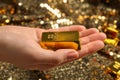 Woman holding shiny gold bar against sequin fabric, closeup Royalty Free Stock Photo