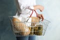 Woman holding shopping basket with products and toilet paper rolls on light blue background. Panic caused by virus Royalty Free Stock Photo