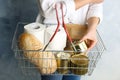 Woman holding shopping basket with products and toilet paper rolls on light blue background. Panic caused by virus Royalty Free Stock Photo