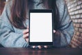 A woman holding and showing black tablet pc with blank white screen in modern cafe with brick wall background Royalty Free Stock Photo