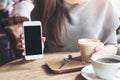 A woman holding and showing white mobile phone with blank black desktop screen with coffee cups on vintage wooden table Royalty Free Stock Photo