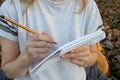 Woman in holding sketchbook and a pencil outdoors. Close-up of hands with notebook and pencil. Drawing, writing, learning