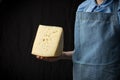 Woman holding slice of cheese wearing blue apron on dark background Royalty Free Stock Photo