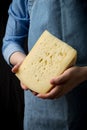 Woman holding slice of cheese wearing blue apron on dark background Royalty Free Stock Photo