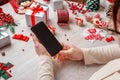 Woman holding smart phone with blank screen for mockup, surrounded by Christmas and New Year decorations Royalty Free Stock Photo