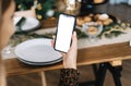 Woman holding a smartphone with a white screen mock up at home near festive table in kitchen Royalty Free Stock Photo
