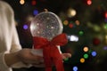 Woman holding snow globe with red bow knot on blurred background, closeup Royalty Free Stock Photo