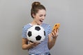 Woman holding soccer ball and smart phone, betting and winning, football match.