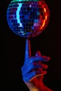 Woman holding spinning disco mirror ball on finger under neon. Glossy silver sphere reflecting light. Retro night party Royalty Free Stock Photo