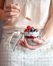 A woman holding a spoon and a mason jar with chai pudding topped with fresh berry fruit