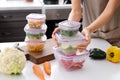 Woman holding stack of plastic containers with fresh vegetables for freezing at table in kitchen Royalty Free Stock Photo