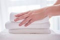 Woman holding stack of white clean bath towels in bedroom interior, copy space. Close up hands of hotel maid with towels.