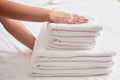 Woman holding stack of white clean bath towels in bedroom interior, copy space. Close up hands of hotel maid with towels.