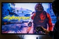 Woman holding a steam controller and playing popular video game Cyberpunk 2077 on a television and PC