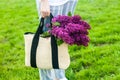 Woman holding straw bag with vivid bunch of lilac flowers