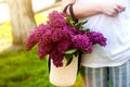 Woman holding straw bag with vivid bunch of lilac flowers