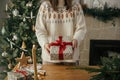 Woman holding stylish christmas gift with red ribbon at wooden table with festive decorations on background of decorated tree and Royalty Free Stock Photo