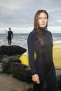 Woman Holding Surfboard With Male Surfer In Background