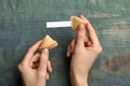 Woman holding tasty fortune cookie and paper with prediction at blue wooden table, top view. Space for text Royalty Free Stock Photo