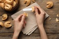 Woman holding tasty fortune cookie and paper with prediction at wooden table, top view. Space for text Royalty Free Stock Photo