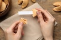 Woman holding tasty fortune cookie and paper with prediction at wooden table, top view. Space for text Royalty Free Stock Photo