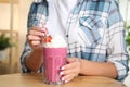 Woman holding tasty fresh milk shake with strawberry at table indoors, closeup Royalty Free Stock Photo