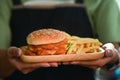 Woman holding tasty homemade fish burger with fried potatoes wooden tray. Royalty Free Stock Photo