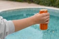 Woman holding tasty open canned beverage near swimming pool, closeup