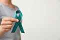 Woman holding teal awareness ribbon against light background Royalty Free Stock Photo