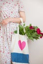 Woman holding a textile bag with beautiful bunch of red peonies. Girl`s hands with bag full of peony flowers Royalty Free Stock Photo