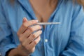 Woman holding thermometer close-up. Blue shirt.