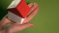 Woman holding toy house with red roof against green background. Real estate agent concept, space for inscriptions Royalty Free Stock Photo
