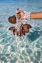 Woman holding tropical branch with necklace made of seashells at sea shore background close up