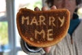 Woman holding up slice of burnt white toast, with the proposal Marry Me