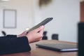 Woman holding and using black mobile phone with laptop on wooden table in office Royalty Free Stock Photo