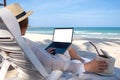 A woman holding and using laptop computer with blank desktop screen while laying down on beach chair and drinking Royalty Free Stock Photo