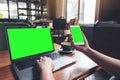 A woman holding and using mockup mobile phone with blank green screen and laptop on wooden table Royalty Free Stock Photo