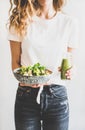 Woman holding vegan superbowl and green smoothie in hands