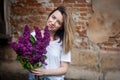 Woman holding a vivid bunch of lilac flowers against brick wall