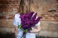 Woman holding a vivid bunch of lilac flowers against brick wall