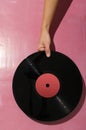 Woman holding vynil record against bright pink background.Hard light