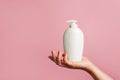 Woman holding white bottle of lotion, soap or shampoo in her hand, pink background with copy space Royalty Free Stock Photo