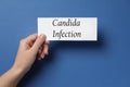 Woman holding white card with phrase Candida Infection on blue background, top view