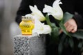 Woman holding white lilies near grey granite tombstone, focus on candle. Funeral ceremony Royalty Free Stock Photo