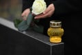 Woman holding white rose near granite tombstone with candle outdoors, closeup. Funeral ceremony Royalty Free Stock Photo