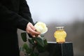 Woman holding white rose near granite tombstone with candle outdoors, closeup. Funeral ceremony Royalty Free Stock Photo