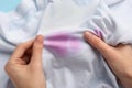 Woman holding white shirt with purple stains on light blue background, closeup